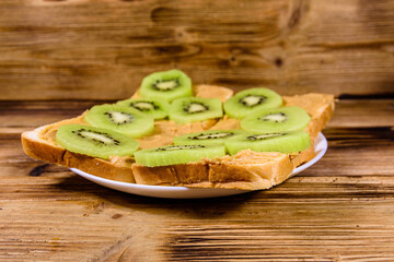 Sandwiches with peanut butter and sliced kiwi fruits in plate on a wooden table