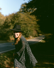 Trendy girl in the woods wearing a black dress and a fedora hat during autumn in Spain.