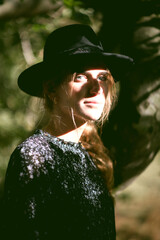 Trendy girl in the woods wearing a black dress and a fedora hat during autumn in Spain.