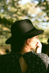 Trendy girl in the woods wearing a black dress and a fedora hat during autumn in Spain.