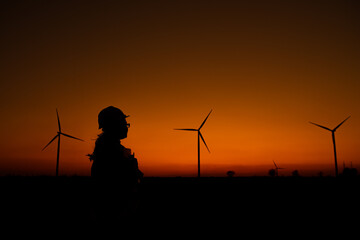 Fototapeta na wymiar Silhouette of women engineer working and holding the report at wind turbine farm Power Generator Station on mountain,Thailand people