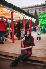 The beautiful young lady standing near Christmas house and keeping two christmas candies 