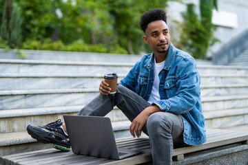 Young african man with laptop sitting on a wooden bench