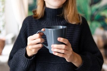 girl holding a blue mug with coffee in a dark sweater close-up