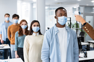 Teacher with contactless thermometer measuring temperature of multiracial students