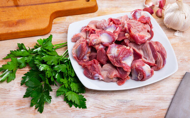 Raw chicken gizzards ready for cooking with fresh vegetables, greens and spices on wooden surface