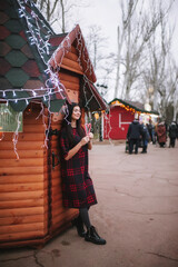 The beautiful young lady standing near Christmas house and keeping two christmas candies 