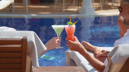 Unrecognizable couple enjoying refreshing drinks lying on sunbeds on poolside - Powered by Adobe
