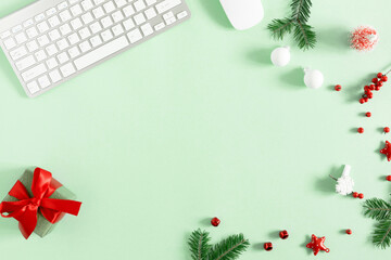 Christmas modern composition. keyboard, gift, fir branches, red berries, Xmas decorations on light green background. Christmas, New Year, winter concept. Flat lay, top view, copy space