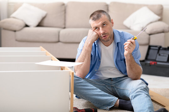Puzzled Man Assembling Furniture Having Trouble Installing Shelf At Home