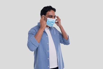 Indian Man Puts on Medical Mask Isolated. Man In Blue Shirt Showing How to put on Medical Mask. Health, Virus, Medical Concept