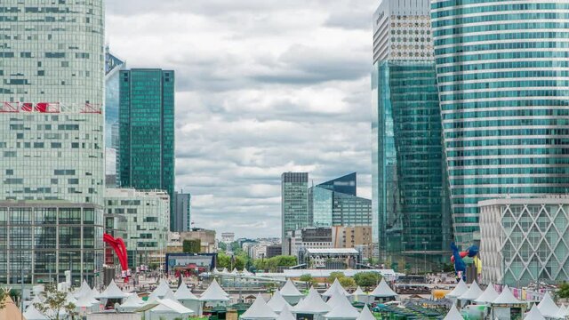 Modern skyscrapers timelapse in famous financial and business district of Paris - La Defense. Cloudy sky at summer day. Arc de triomphe visible on the horizon.
