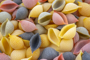 Colored Italian pasta in the shaped of seashells with yellow, pink, and purple colors. Textured background. Macro close up, selective focus.