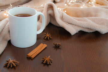 Living room details in winter. Close-up of a white cup with an infusion on a wooden table with anise and cinnamon, and a cream colored blanket. Homey winter concept.
