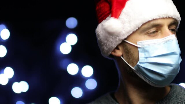Young bearded European man in Santa hat, medical mask and gloves is dancing. Happy European man wearing a Santa hat and a medical mask is dancing to the music on a bokeh background. video close-up.