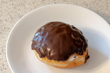 A chocolate cover cream filled donut on a white plate atop a kitchen counter.