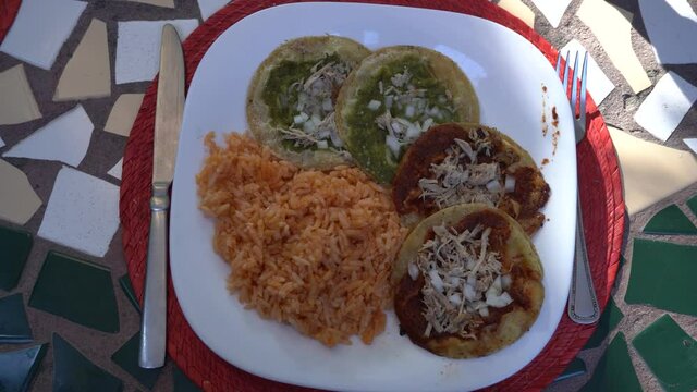 Close up shot of a plate with traditional mexican food chalupas and red rice on a table outdoors during a sunny day