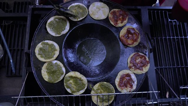 Top view wide shot of mexican dish chalupas being prepared with red and green salsa, onion and meat in a hot comal