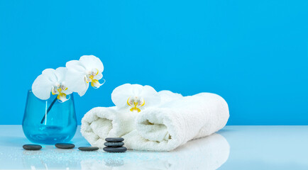 Spa Moth orchid with soft towel and massage stones setting. Zen pebbles balance. Spa and healthcare concept on blue Background