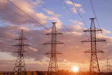 Electric powerlines. High voltage power lines, pylons over sunset with orange sun and sunlight