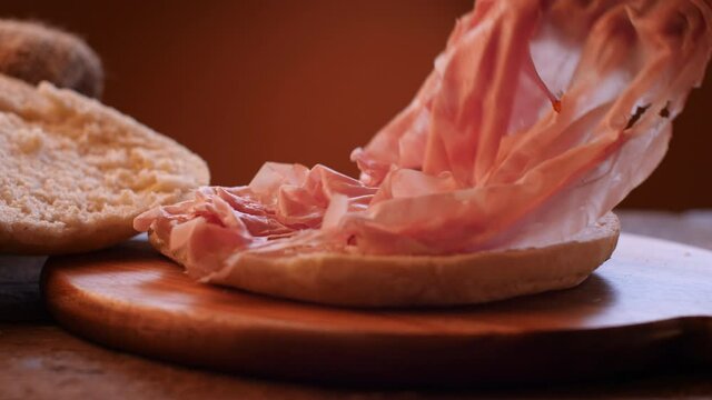 Italian mortadella sandwich on wooden cutting board. Rustic scene describing the filling of bread with sliced mortadella. Dolly and slow motion movement.