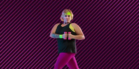 Young caucasian plus size female model's training on dark purple background in neon. Neoned modern artwork, cover, flyer designed. Concept of sport, healthy lifestyle, body positive, equality.