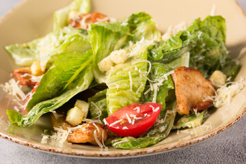 Caesar salad with chicken. Romano lettuce, chicken fillet, tomatoes, croutons, parmesan cheese and sauce in a plate on a light background. Restaurant menu. Background image, copy space
