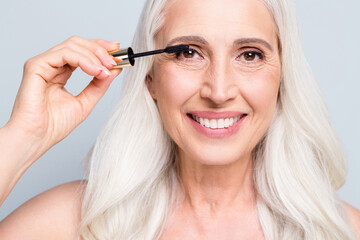 Close up photo of beautiful retired woman face applying brush eyelashes cover extra long lashes isolated grey color background