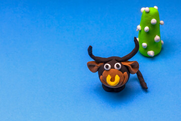 Cheerful smiling plasticine bull and plasticine fir tree with toys on a light blue background with copy space.
