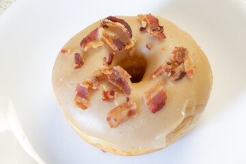 Maple cream glazed donut with bacon bits on top isolated on a white plate.