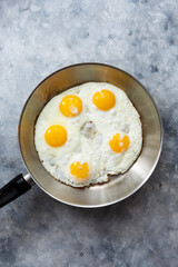 Fried eggs in iron frying pan on dark background, top view.
