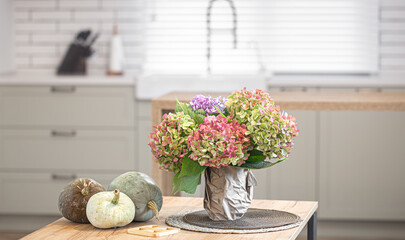 A bouquet of hydrangeas and pumpkins on the kitchen table as part of autumn home decor.