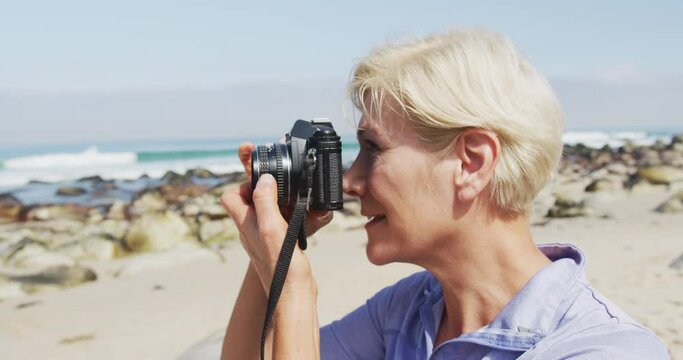 Senior hiker woman taking pictures using digital camera on the beach.