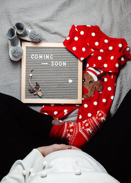 Pregnant Woman Sitting With A Coming Soon Baby Announcement Sign. Coming Soon Christmas Concept. Pregnancy Belly. Blank Space.