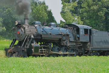 Naklejka premium Close Up of an Antique Steam Passenger Train Puffing along Amish Countryside with Green Fields