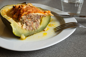 A piece of homemade stuffed zucchini baked with meat, onions, eschalot, garlic, eggs, herbs, cheese on a white plate on a gray table