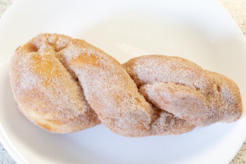 A twisted donut covered in powder sugar on a plate ready to be served.
