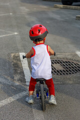 Adorable Asian kid boy (Toddler age 1-year-old), Wearing a Safety Helmet and Learning to Ride a Balance Bike in the Play Space.