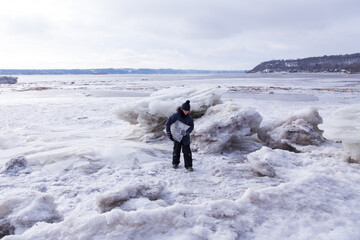 Horizontal shot of young girl carrying a large ice chunk on the banks of partly frozen St. Lawrence river in winter, Cap-Rouge area, Quebec City, Quebec, Canada