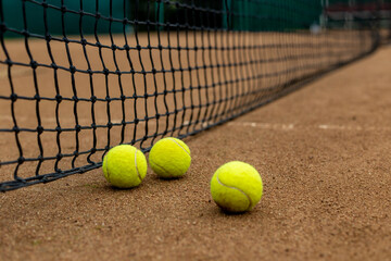 Three tennis balls lie side by side on a red clay court along the playing net.