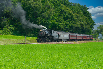 Antique Steam Passenger Train Puffing Lots of Black Smoke along Amish Countryside with Green Fields
