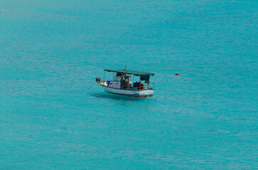 Simos bay at Elafonissos, south Greece. 
A peacefull scenery with turquoise water. A fishing boat stands alone on the water. A photo taken from a hill with zoom, isolating the boat.