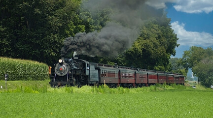 Fototapeta na wymiar Antique Steam Passenger Train Puffing along Amish Countryside with Green Fields