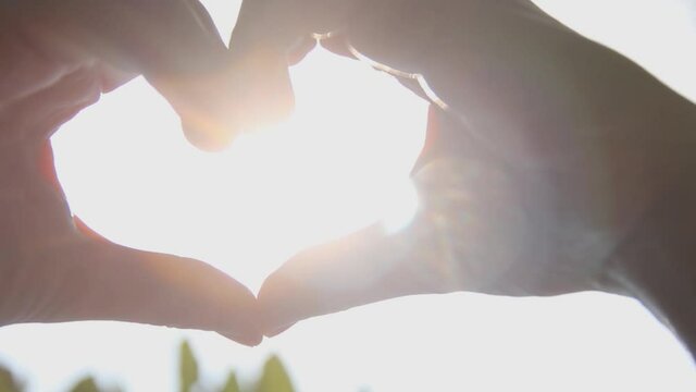 A shot of a heart symbol is created from a woman's hands on a background of sun rays