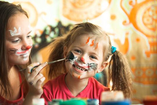 Two little cute sisters playing with face painting.