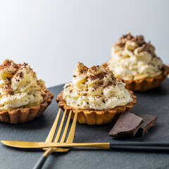 banoffi pie with white cream and chocolate chips, on a stone tray with a fork and knife