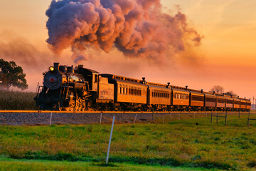 View of Golden Steam Passenger Train at Sunrise Traveling Thru Amish Countryside with lots of Smoke and Steam