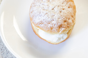 A powdered vanilla cream filled donut on a white plate waiting to be served.