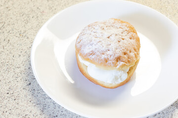 A powdered vanilla cream filled donut on a white plate waiting to be served.