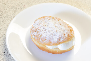 A powdered vanilla cream filled donut on a white plate waiting to be served.